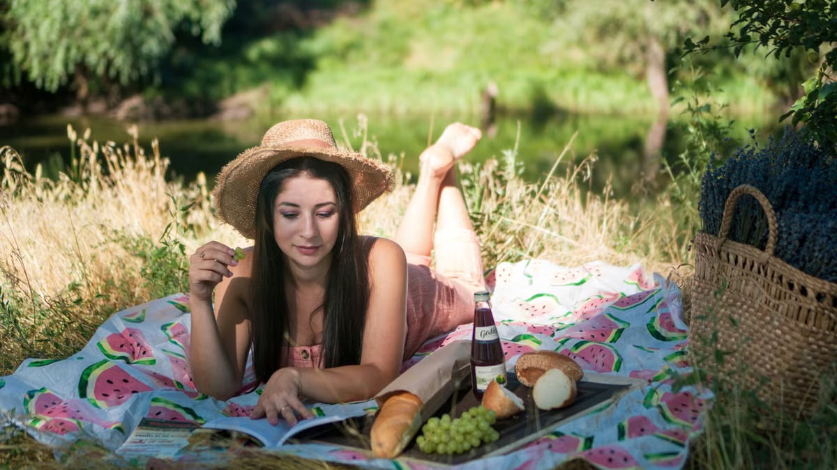 Woman enjoying a tranquil summer picnic by the river with food and nature.